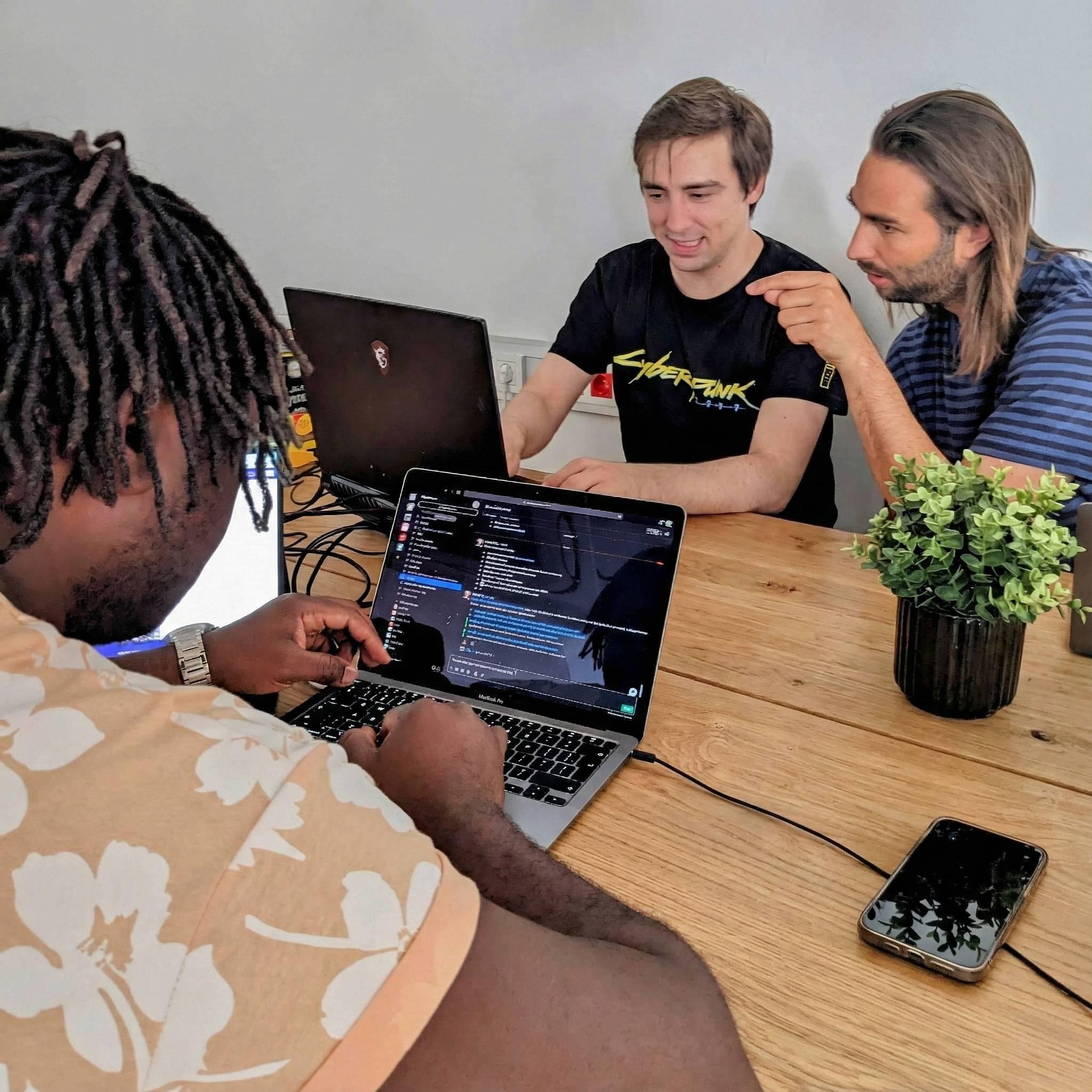 Three men collaborating on coding an app with a laptop in a modern tech workspace.