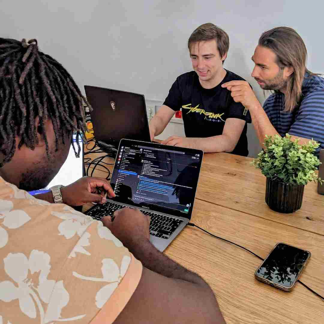 Three men collaborating on coding an app with a laptop in a modern tech workspace